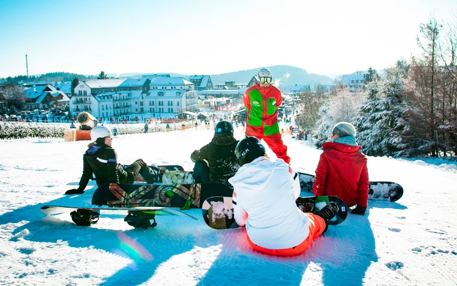 Snowboardlehrer erklärt Schülern etwas zum Snowboard fahren.