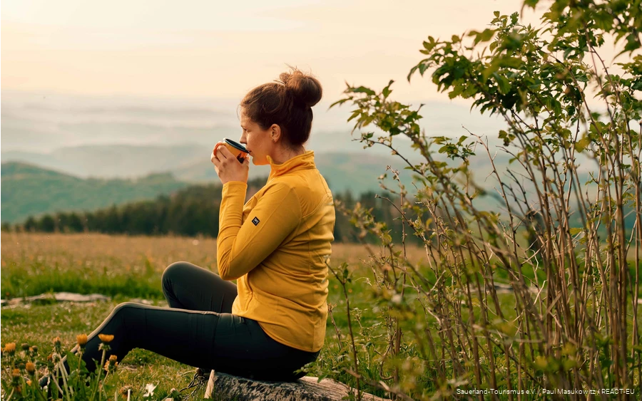 Een wandelaar geniet van haar pauze met een kopje koffie en uitzicht over het landschap.