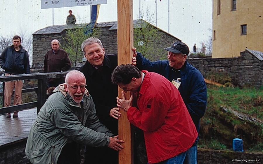 Vier Männer stellen erfreut den ersten Wegweiser des Rothaarsteigs im Rahmen seiner Eröffnung auf. Auf dem Schild sind die Distanzen zu den beiden Start-/Endpunkten des Fernwanderwegs zu sehen.