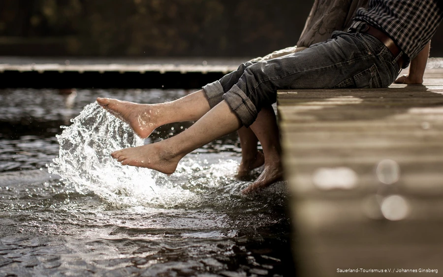 Two excursionists dip their feet into the clear water of a Sauerland lake.