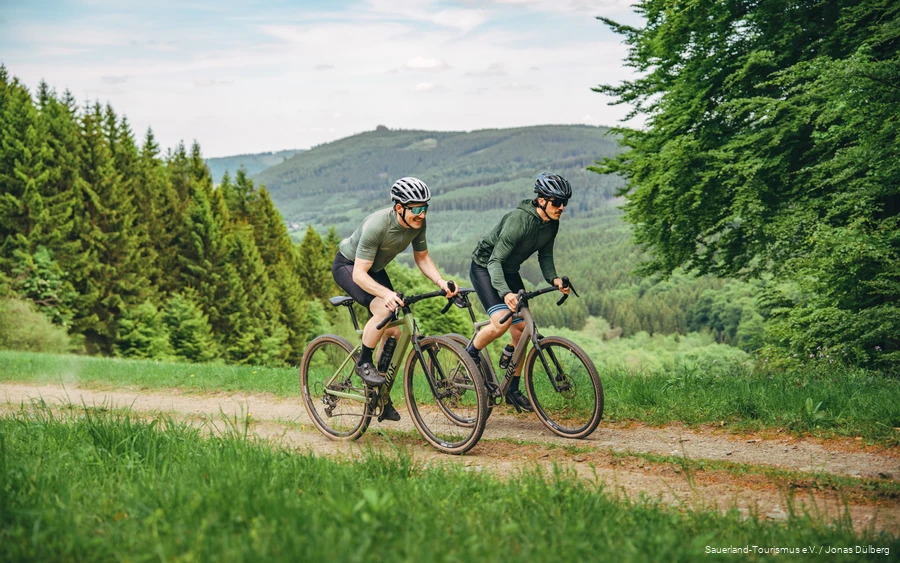 Zwei Gravelbiker fahren einen leichten Anstieg hinauf. Sie tragen grün und auch die Landschaft erstrahlt in verschiedenen Grüntonen.