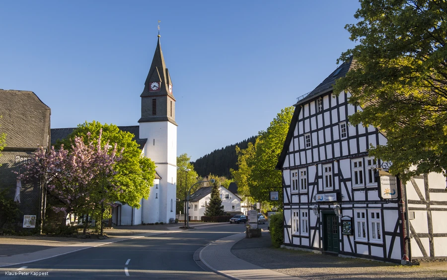 Eine Kirche an einer Straße mit einem Fachwerkhaus im Vordergrund. Eine Kirche an einer Straße mit einem Fachwerkhaus im Vordergrund.