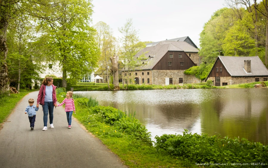 Eine Mutter ist mit zwei Kindern auf dem Gelände der Wendener Hütte unterwegs. Sie spazieren am Teich entlang.