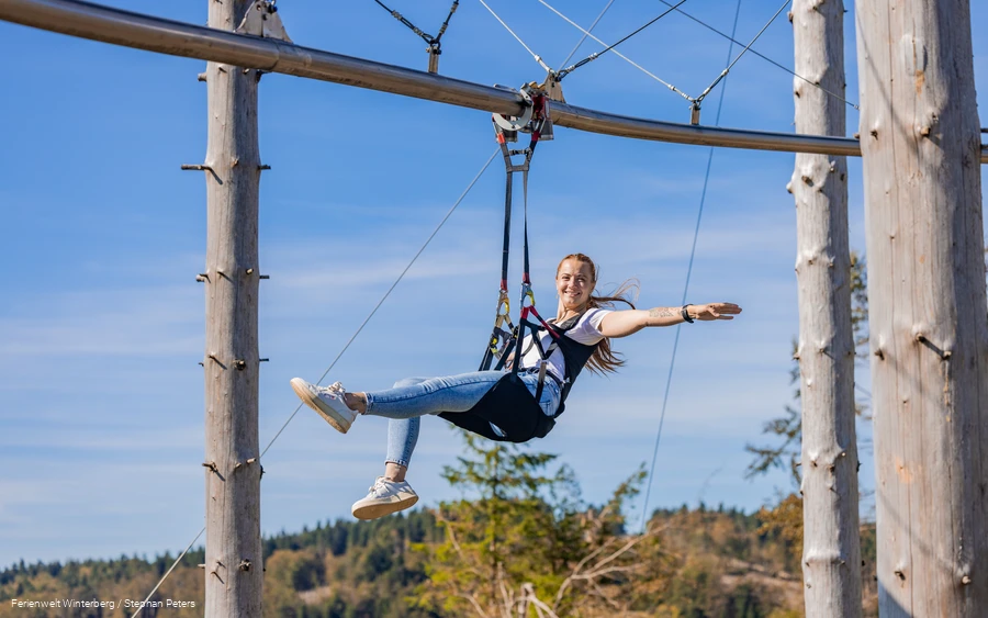 Eine Frau hängt an einem Sitzgurt an einer Metallschiene und breitet die Arme aus.