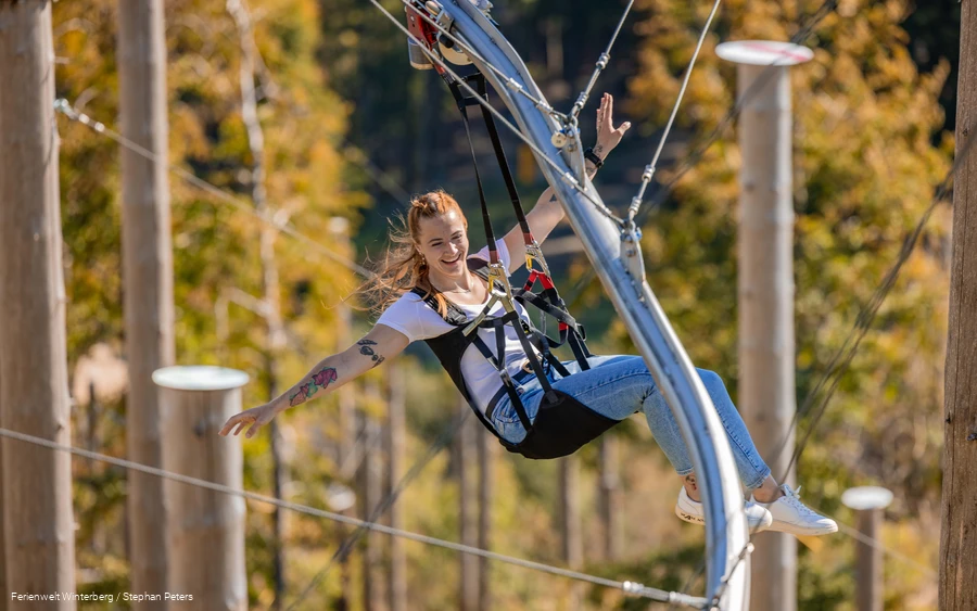 Eine Frau fliegt in einem Sitzgurt sitzend an einer Metallschiene den Berg hinab.