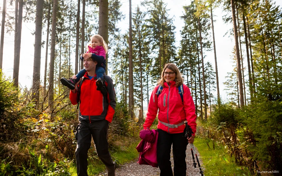 Een gezin tijdens een wandeling door het herfstige landschap van Sauerland. De vader draagt zijn dochter op zijn schouders.