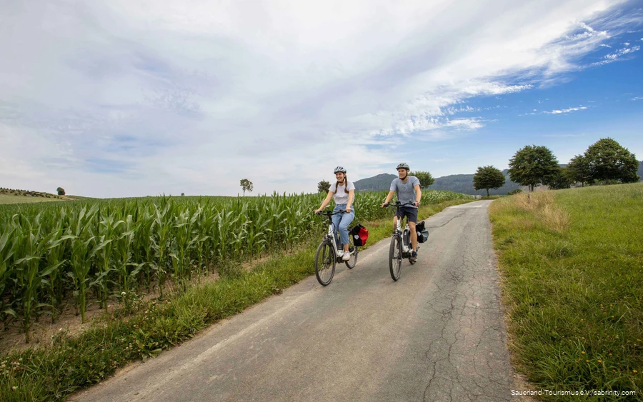 A couple cycle leisurely along a cycle path through green meadows.