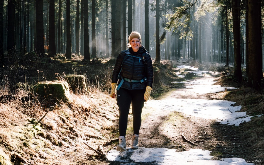 Paulien Outdoor Inspiratie Bloggerin Paulien wandert durch einen Fichtenwald mit kleinen Flecken von Schnee auf dem Waldweg.