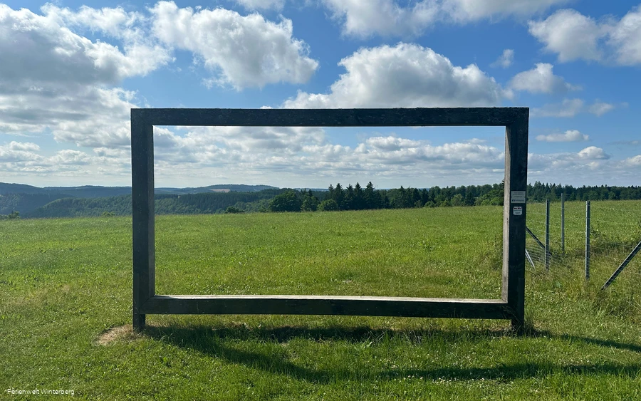 Landschaftsrahmen aus Holz mit Blick auf Wiesen und Wälder.