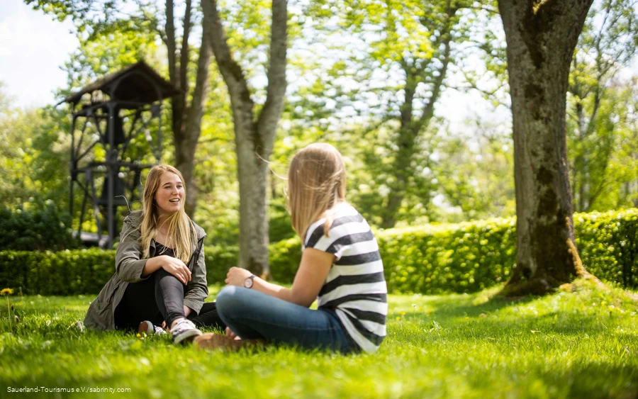 Zwei Freundinnen sitzen auf der Wiese und unterhalten sich.