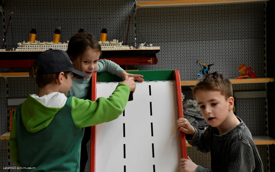 Drei Kinder spielen im Legomuseum mit einer Art Rampe.