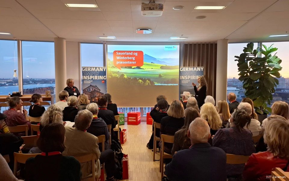 A large group of people are watching a presentation. Next to them are two women who are giving a presentation.
