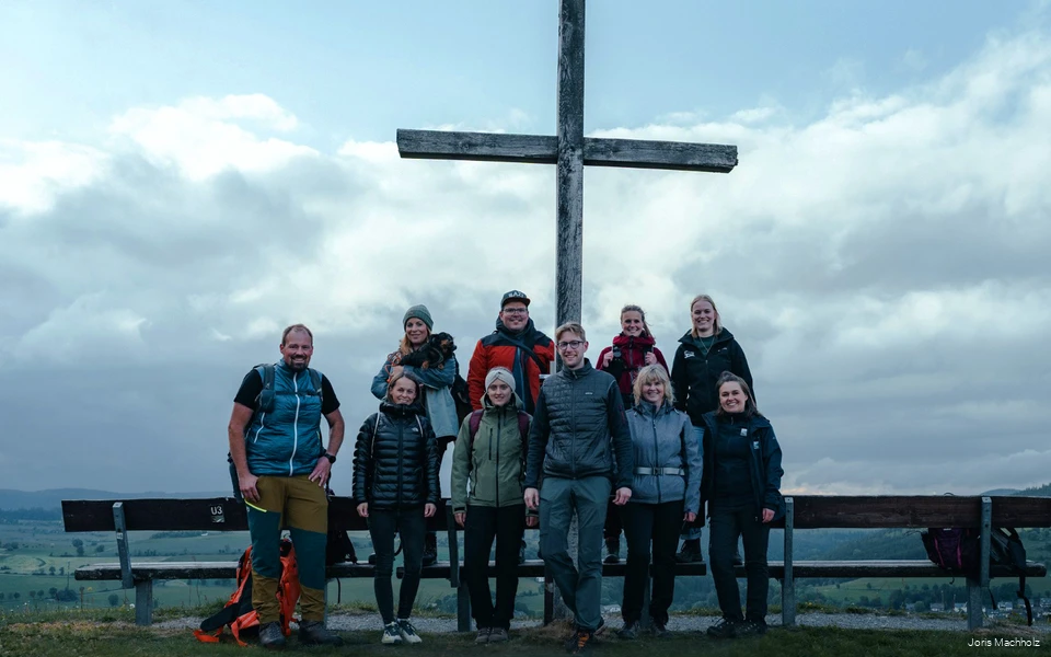 Die Teilnehmer des InstaHikes stehen vor dem Gipfelkreuz Usselner Kreuz. Der Himmel ist wolkenbehangen.