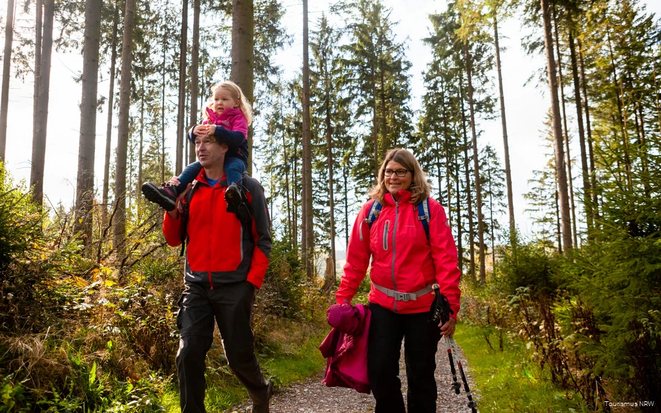 A family on a hike through the autumnal Sauerland landscape. The father carries his daughter on his shoulders.