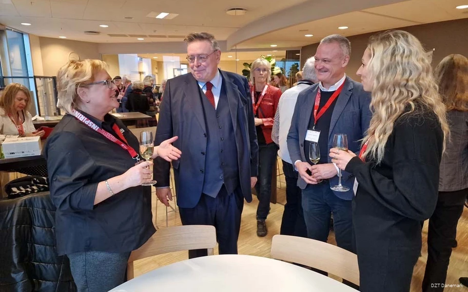 Zwei Frauen unterhalten sich mit zwei Männern. Sie haben Sektgläser in der Hand und Ausweise umhängen.