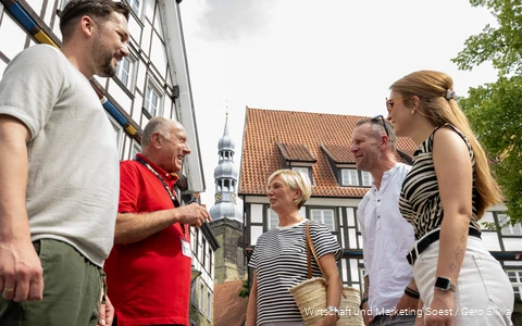 Einblick in eine Stadtführung in Soest mit einem Guide in rotem T-Shirt. Im Hintergrund sind eine der zahlreichen Soester Kirchen und Fachwerkhäuser zu sehen.