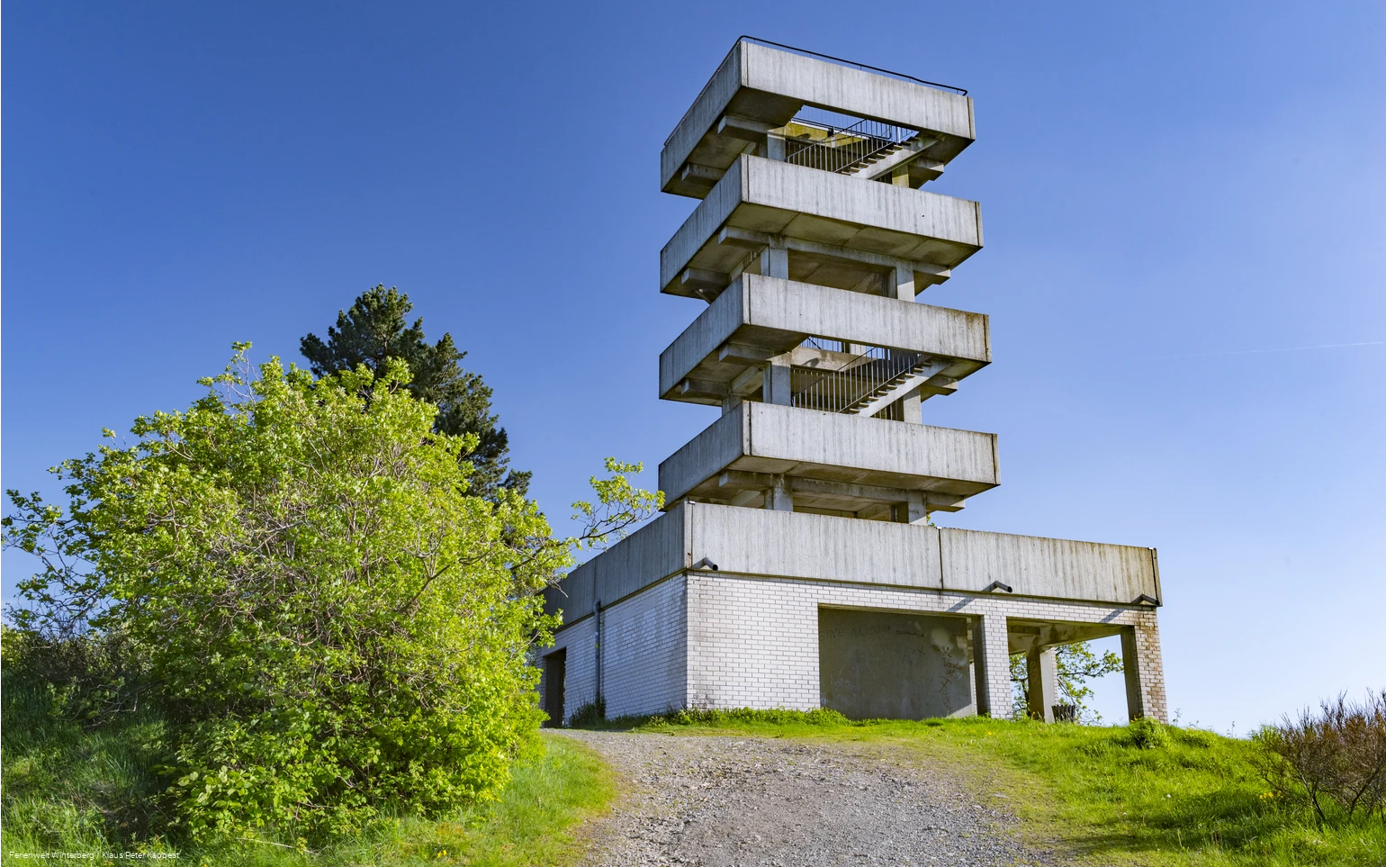 Turm aus Beton mit mehreren Etagen und Treppenaufgängen vor blauem Himmel.