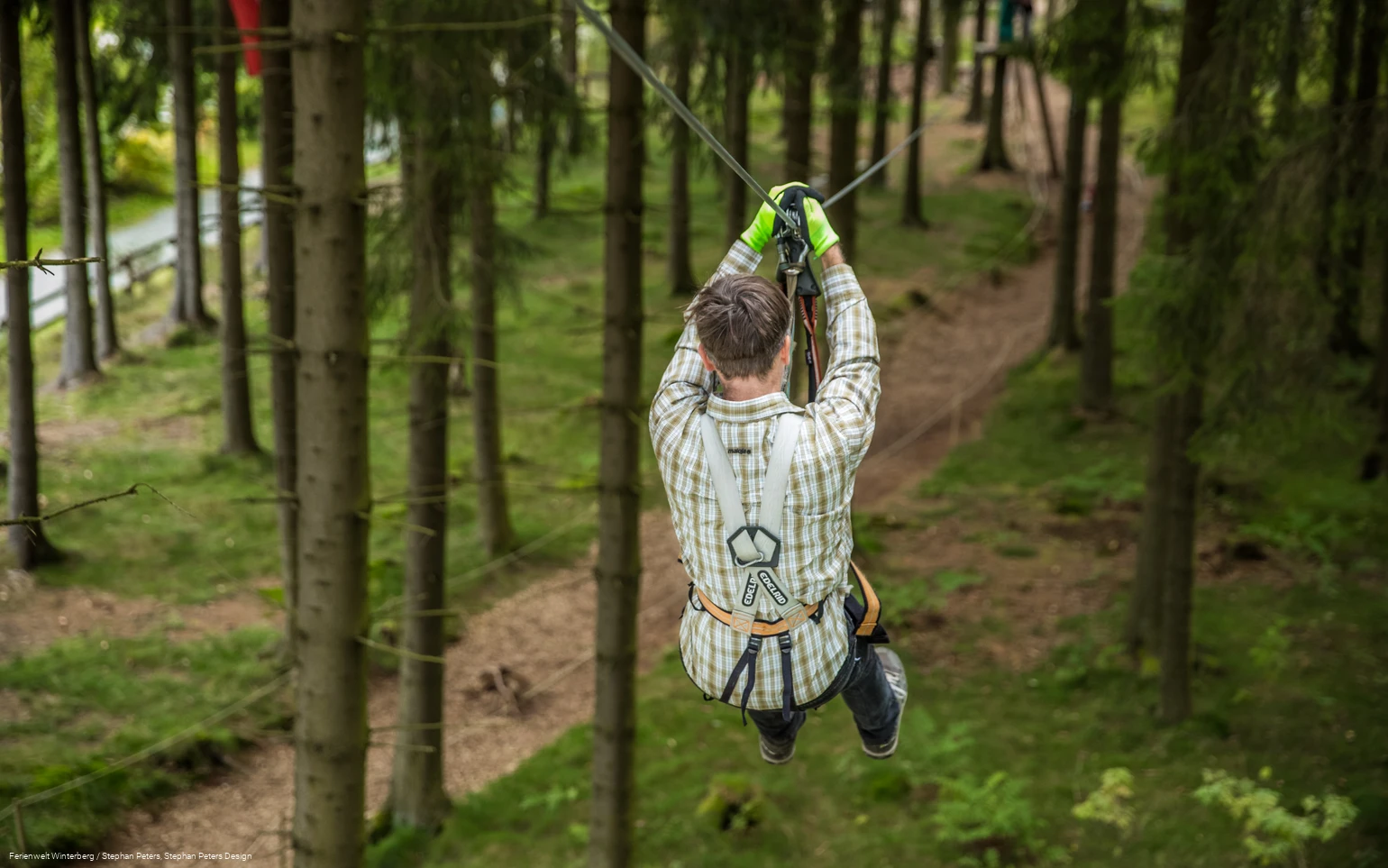Eine Person fliegt an einem Gurt und Seil gesichert von einem Baum zum nächsten.