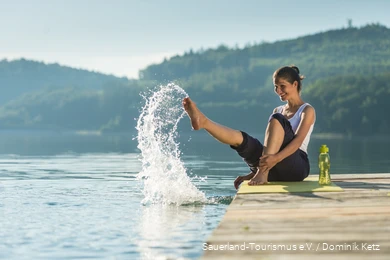 Eine Frau sitzt auf einem Steg am Hennesee und spritzt mit Wasser.