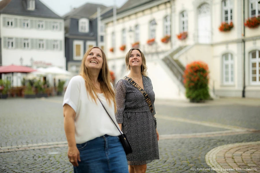 Zwei junge Frauen schauen strahlend hoch zu den Gebäuden. Der verschwommene Hintergrund zeigt den Lippstädter Rathausplatz.