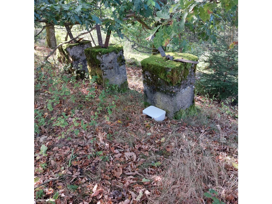 Eine Kiste mit dem Gipfelbuch liegt gut versteckt hinter einem gro&szlig;en Stein