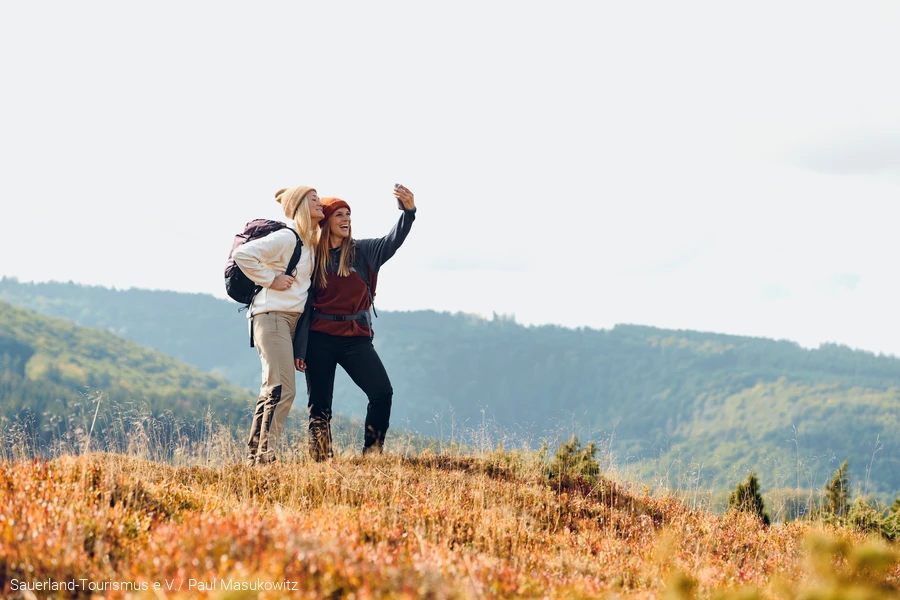 Two women take a selfie in front of a beautiful wooded backdrop