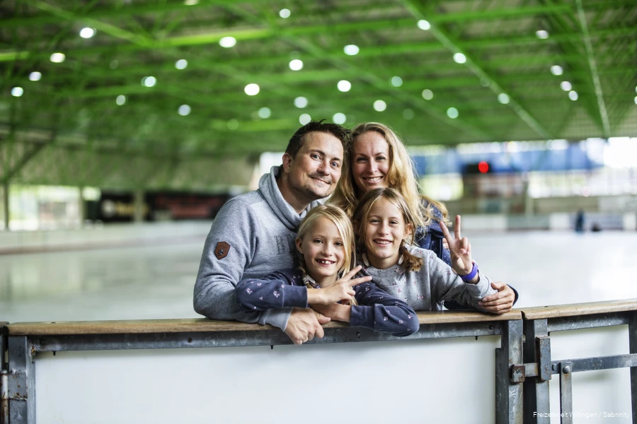 Mutter, Vater und zwei Töchter posieren am Rand der Eislauffläche für ein Foto.
