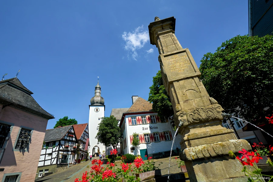 Der Marktplatz in Arnsberg ist umringt von alten Häusern, teils Fachwerkhäuser. In der Mitte steht ein Brunnen und den Berg hinauf die Kirche.