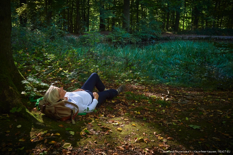 A woman lies in a forest clearing and enjoys nature.