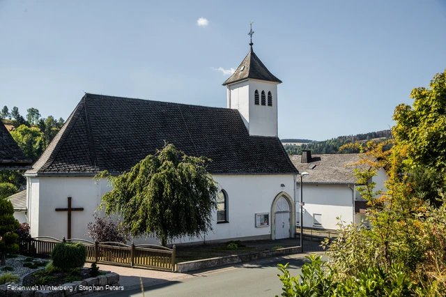 Eine Kirche vor blauem Himmel und einem Baum im Vordergrund.