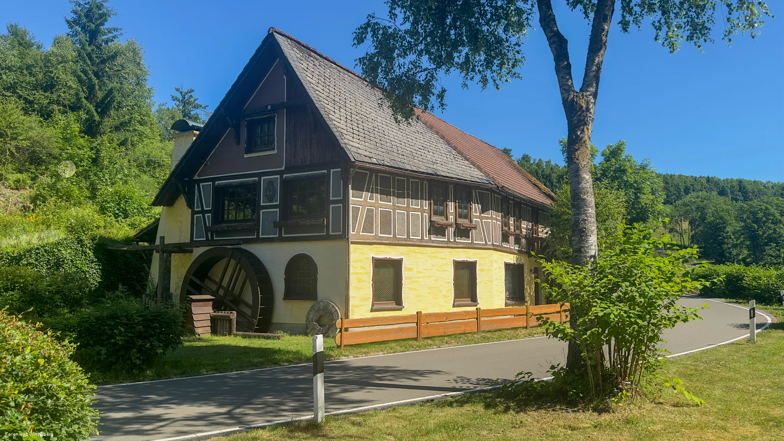Ein altes Gebäude mit Fachwerk und einem Wasserrad an der seitlichen Hauswand.