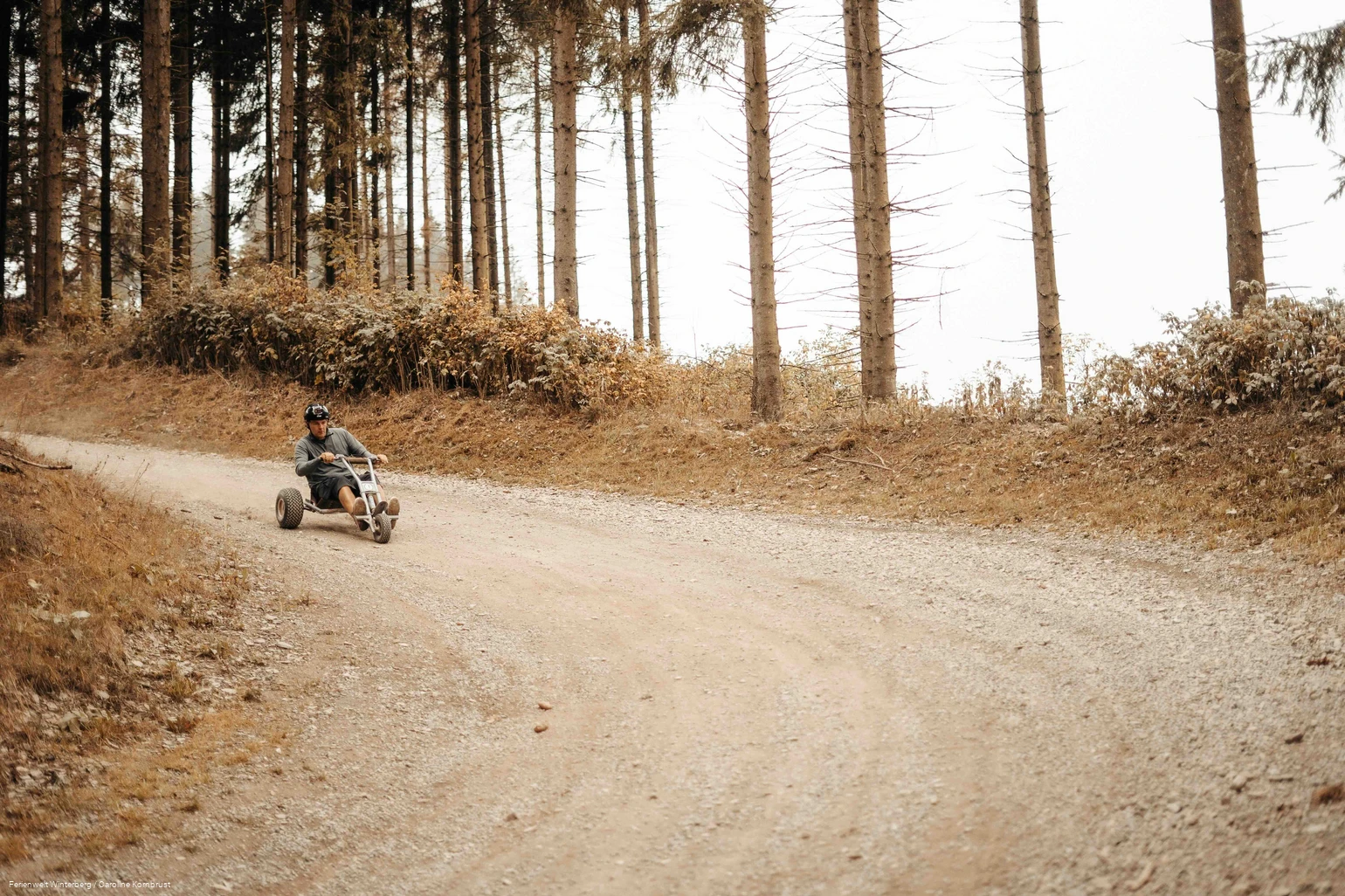 Eine Person fährt mit einem Mountaincart, Fahrzeug mit drei Rädern und einem Lenker, durch eine Kurve einen Waldweg hinab. Eine Person fährt mit einem Mountaincart, Fahrzeug mit drei Rädern und einem Lenker, durch eine Kurve einen Waldweg hinab.