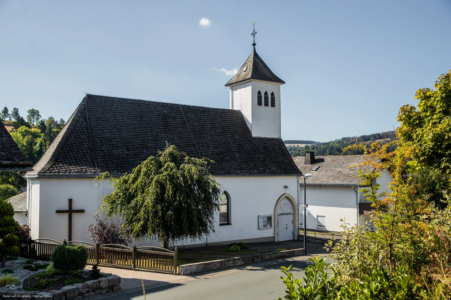 Eine Kirche vor blauem Himmel und einem Baum im Vordergrund.