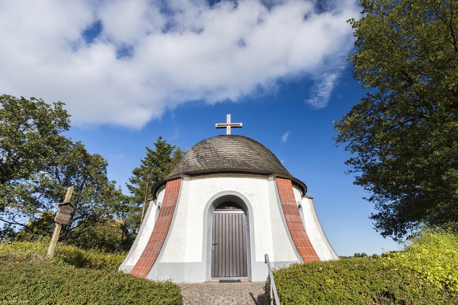 Eine Kapelle umgeben von Bäumen vor blauem Himmel.