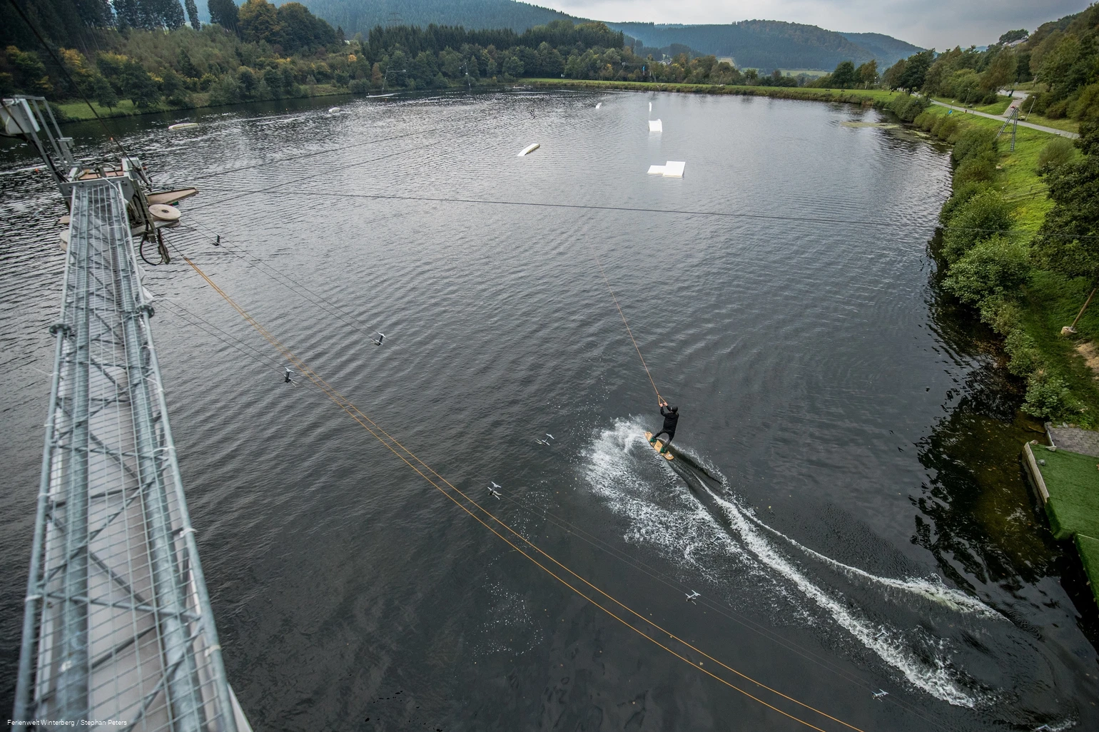Ein Wasserskifahrer wird an einem Seil über den See gezogen.