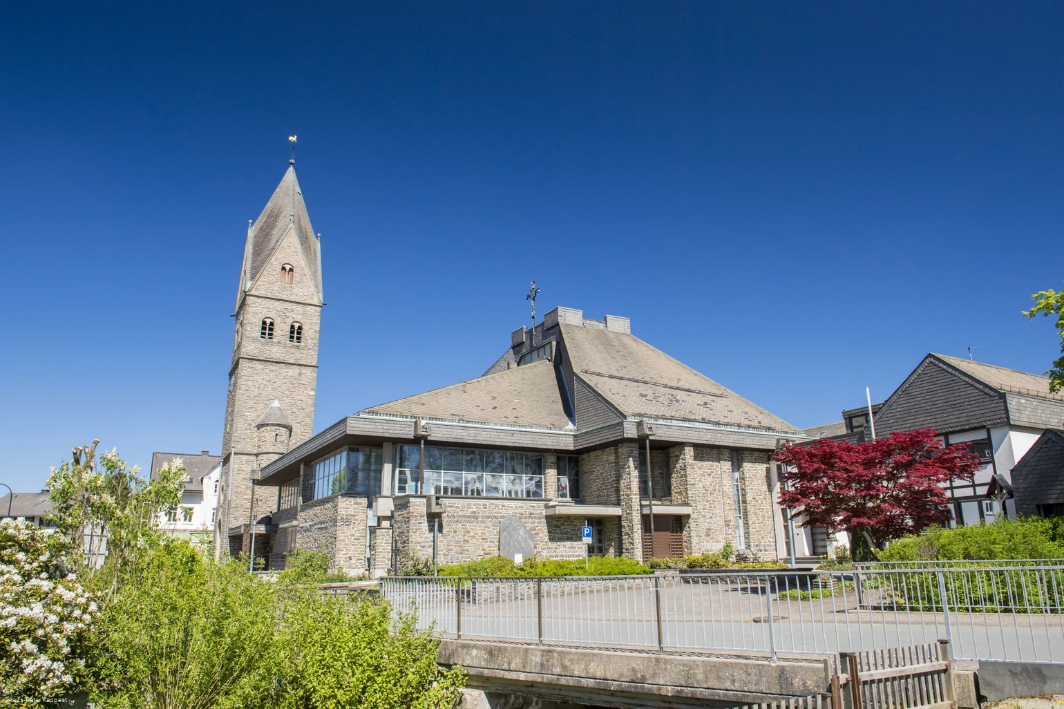 Eine Kirche vor blauem Himmel mit Bäumen und Sträuchern im Vordergrund.